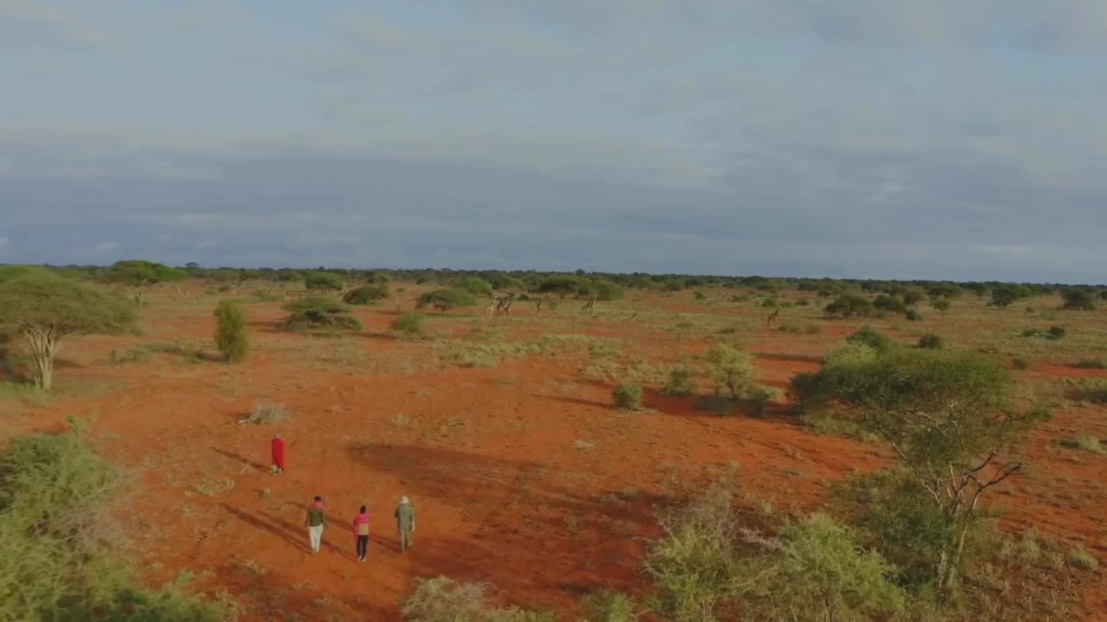 Guests walking across the red-earth plains of a Kenyan safari landscape